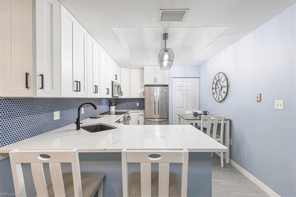 809 Augusta Boulevard, Unit 3 Naples, FL 34113 - Photo 15 of 32 Kitchen with a tray ceiling, decorative backsplash, stainless steel appliances, a kitchen breakfast bar, and white cabinetry