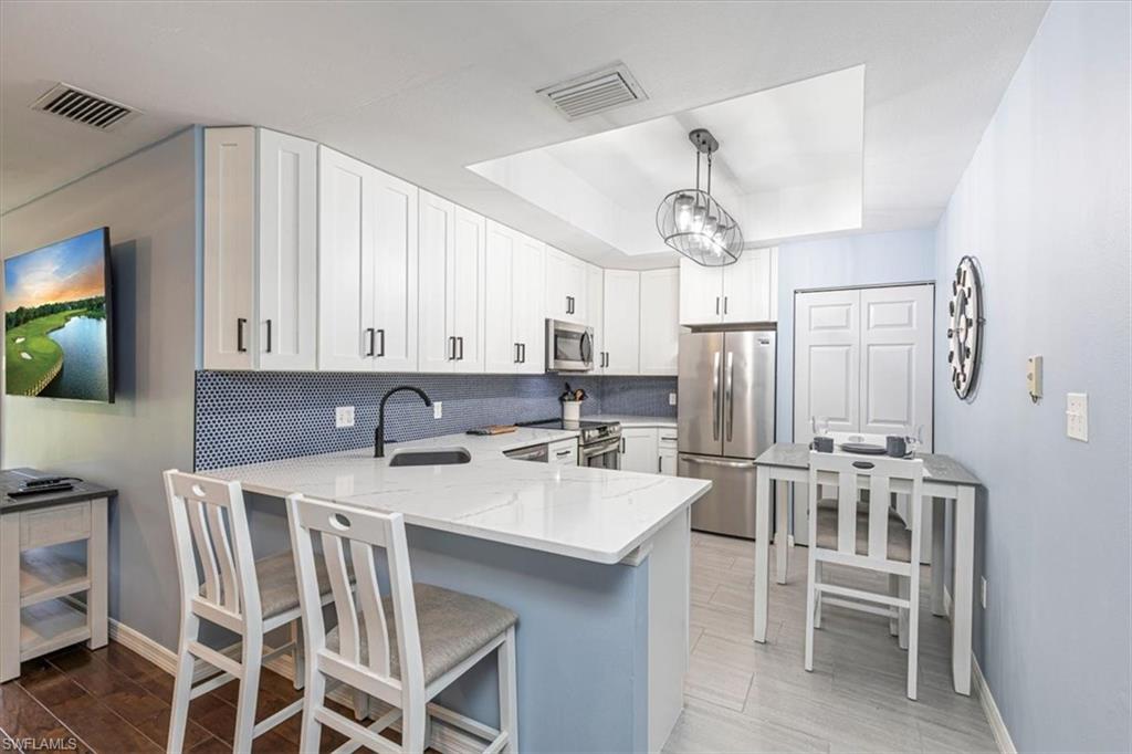 809 Augusta Boulevard, Unit 3 Naples, FL 34113 - Photo 16 of 32 Kitchen featuring a raised ceiling, white cabinetry, stainless steel appliances, light stone counters, and light wood-style floors
