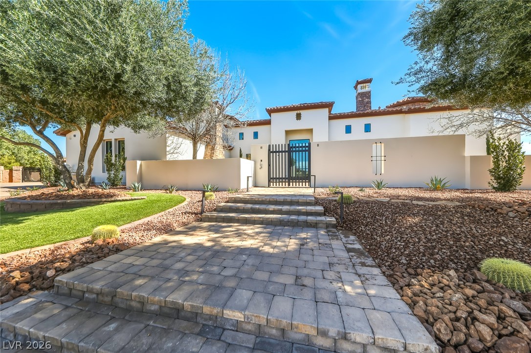 1140 Julie Road Henderson, NV 89002 - Photo 3 of 38 A grand entrance with paver steps leads to a private courtyard gate, flanked by desert-friendly landscaping and mature trees.