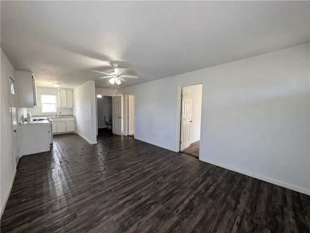 a view of an empty room with wooden floor and a kitchen