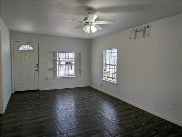 an empty room with wooden floor chandelier fan and windows