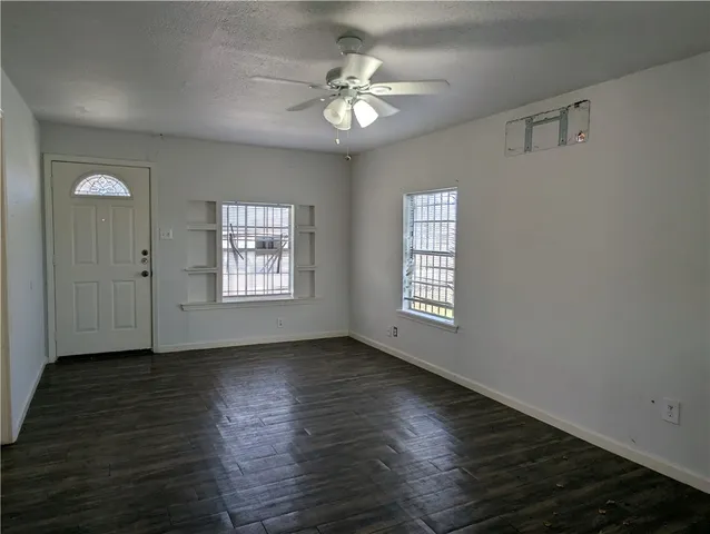 an empty room with wooden floor chandelier fan and windows
