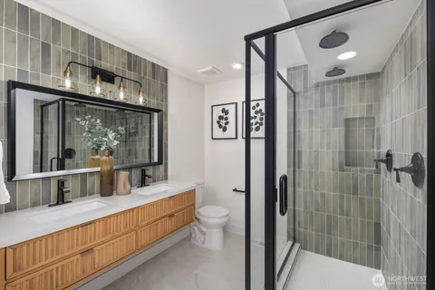 a bathroom with a double vanity sink a toilet a mirror and shower