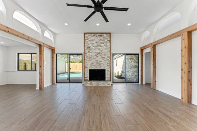 an empty room with wooden floor a ceiling fan a fireplace and windows