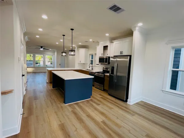 a large kitchen with stainless steel appliances granite countertop a refrigerator a sink dishwasher a stove and a dining table with wooden floor
