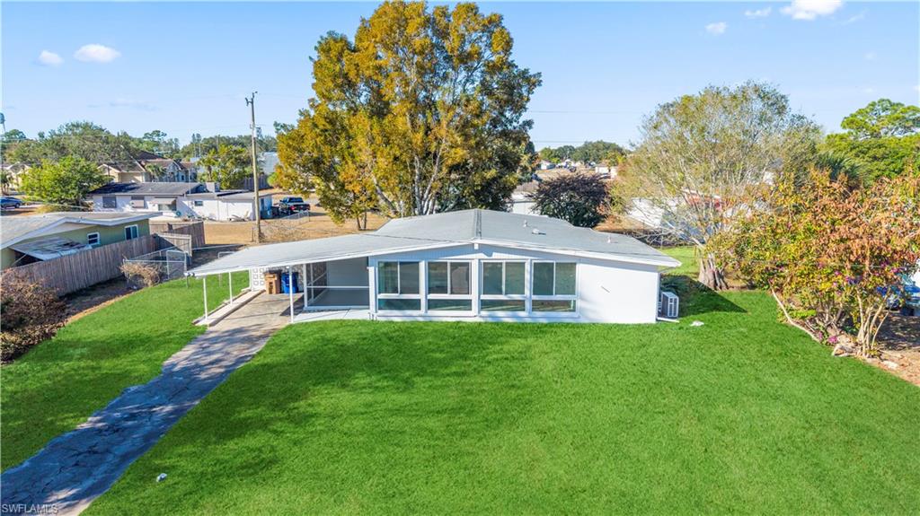 105 Oregon Road North Lehigh Acres, FL 33936 - Photo 1 of 17 Back of property featuring a sunroom, a carport, a yard, and concrete driveway