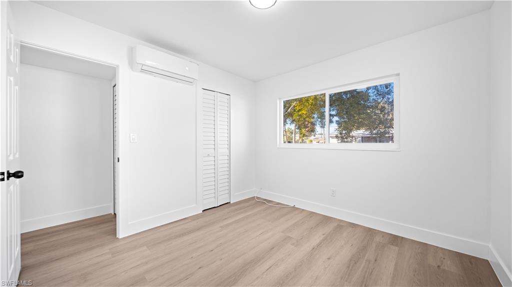 105 Oregon Road North Lehigh Acres, FL 33936 - Photo 14 of 17 Unfurnished bedroom with light wood finished floors, a wall mounted mini split, and a closet