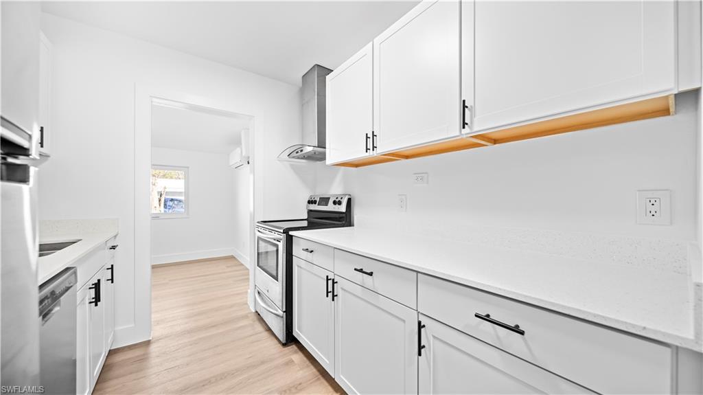 105 Oregon Road North Lehigh Acres, FL 33936 - Photo 4 of 17 Kitchen featuring stainless steel appliances, white cabinets, light wood-style floors, and light stone counters