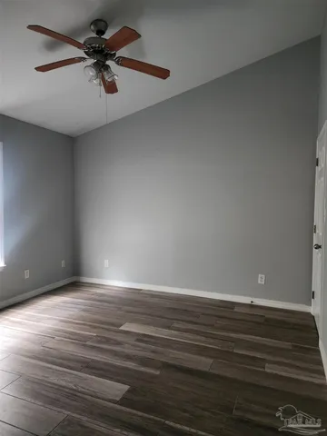 a view of an empty room with wooden floor and a ceiling fan