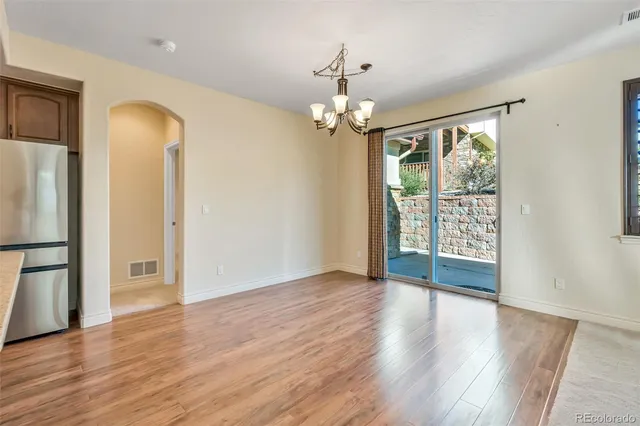 an empty room with wooden floor chandelier and windows
