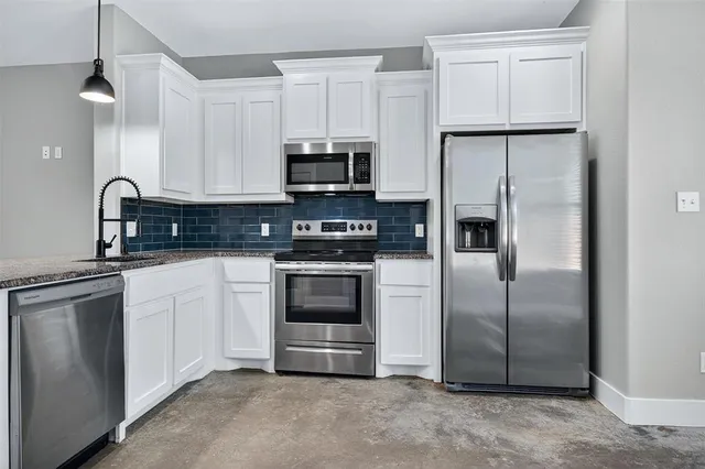 a kitchen with stainless steel appliances granite countertop a refrigerator a stove a sink and white cabinets