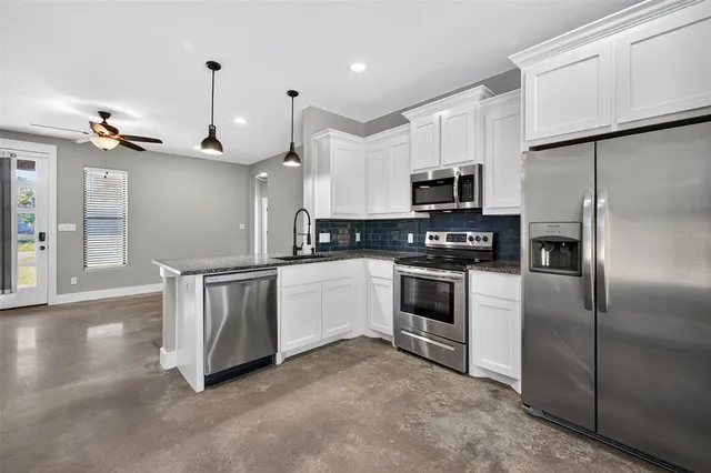 a kitchen with granite countertop a refrigerator a sink and white cabinets