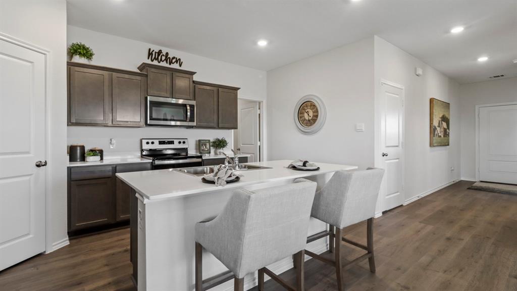 636 Dunham Road Nevada, TX 75173 - Photo 20 of 31 Kitchen featuring dark wood-finish cabinetry, stainless steel appliances, a white countertop island with seating, and wood-finish flooring