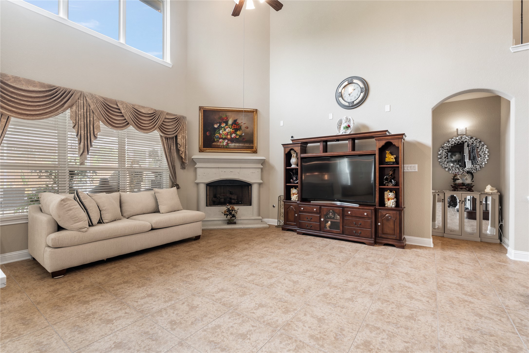 5802 Layton Meadows Lane Spring, TX 77379 - Photo 9 of 42 Living room with fireplace — first angle. Soaring two-story ceilings, clerestory windows, white fireplace mantle, draped windows, oil painting above the mantle, and open sightlines to the dining area and kitchen. Elegant and spacious.