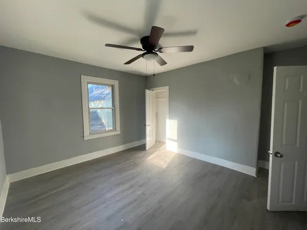 an empty room with wooden floor chandelier fan and windows