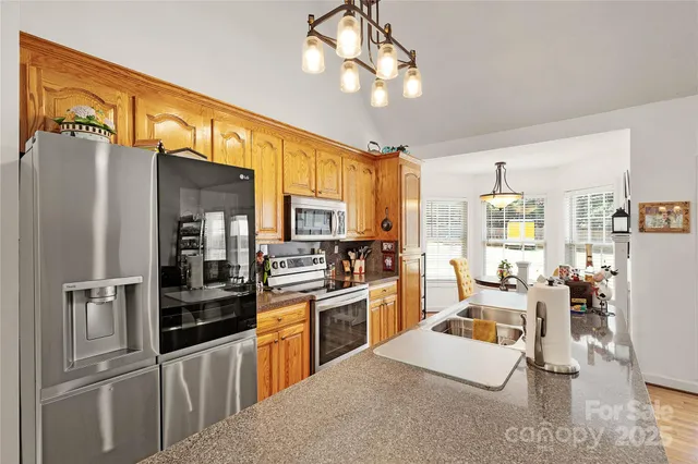 a kitchen with stainless steel appliances granite countertop a refrigerator a stove a sink a dining table and chairs with wooden floor