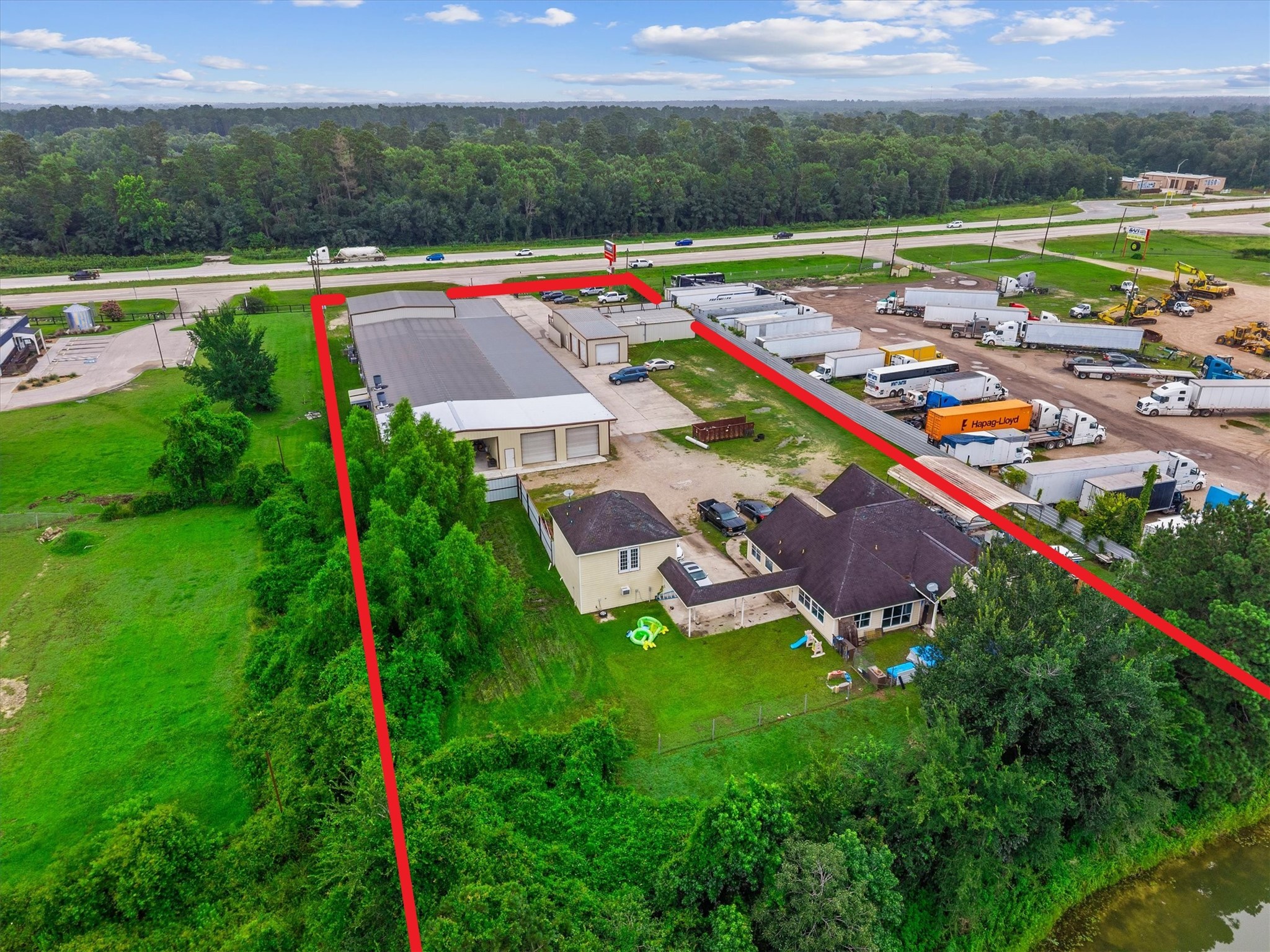 11066 Sh 242 Conroe, TX 77385 - Photo 7 of 21 This aerial photo showcases a property with a mix of residential and commercial use. The area includes a house with a fenced yard and adjacent storage or warehouse buildings. It's situated near a busy road and surrounded by greenery, offering both accessibility and space.