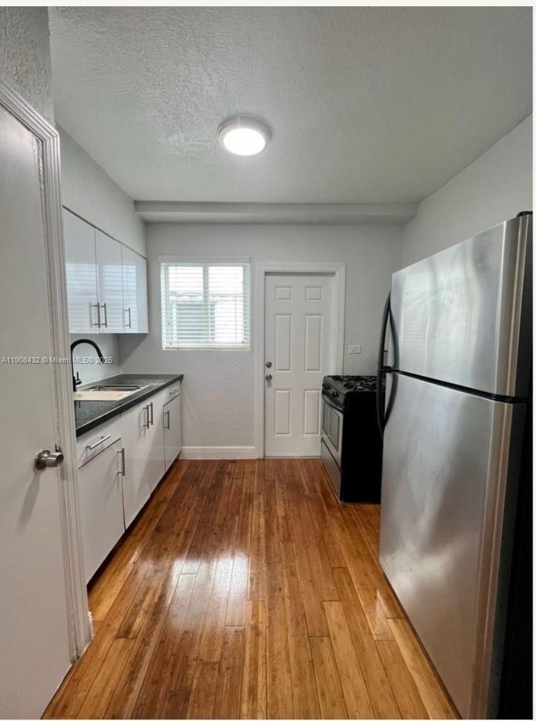 7315 Carlyle Avenue, Unit 10 Miami Beach, FL 33141 - Photo 4 of 9 a kitchen with a refrigerator a sink and dishwasher with wooden floor