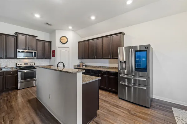 a kitchen with stainless steel appliances granite countertop a stove top oven a sink and dishwasher a refrigerator with wooden floors
