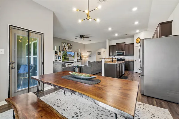 a kitchen with stainless steel appliances kitchen island granite countertop a refrigerator a stove top oven a sink a dining table and chairs with wooden floor