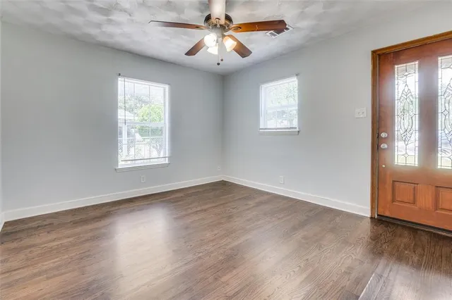 an empty room with wooden floor chandelier fan and windows