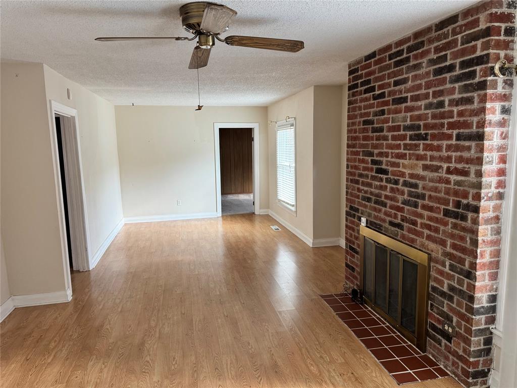 1824 North Binkley Street Sherman, TX 75092 - Photo 4 of 19 Unfurnished living room featuring a textured ceiling, light wood-style floors, a brick fireplace, and a ceiling fan