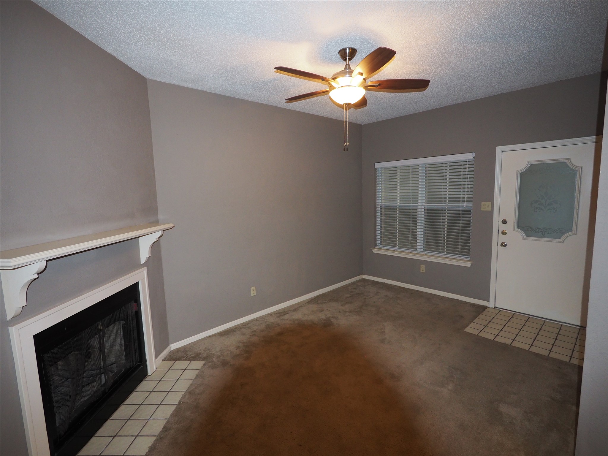 2508 Enfield Road, Unit 10 Austin, TX 78703 - Photo 4 of 17 Living area featuring a fireplace with a white mantel, ceiling fan with light fixture, window with blinds, and an entry door with decorative glass