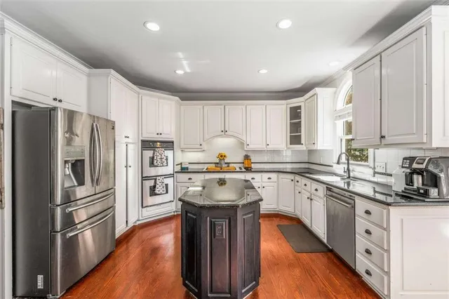 a kitchen with stainless steel appliances granite countertop a stove top oven a sink dishwasher a dining table and chairs with wooden floor