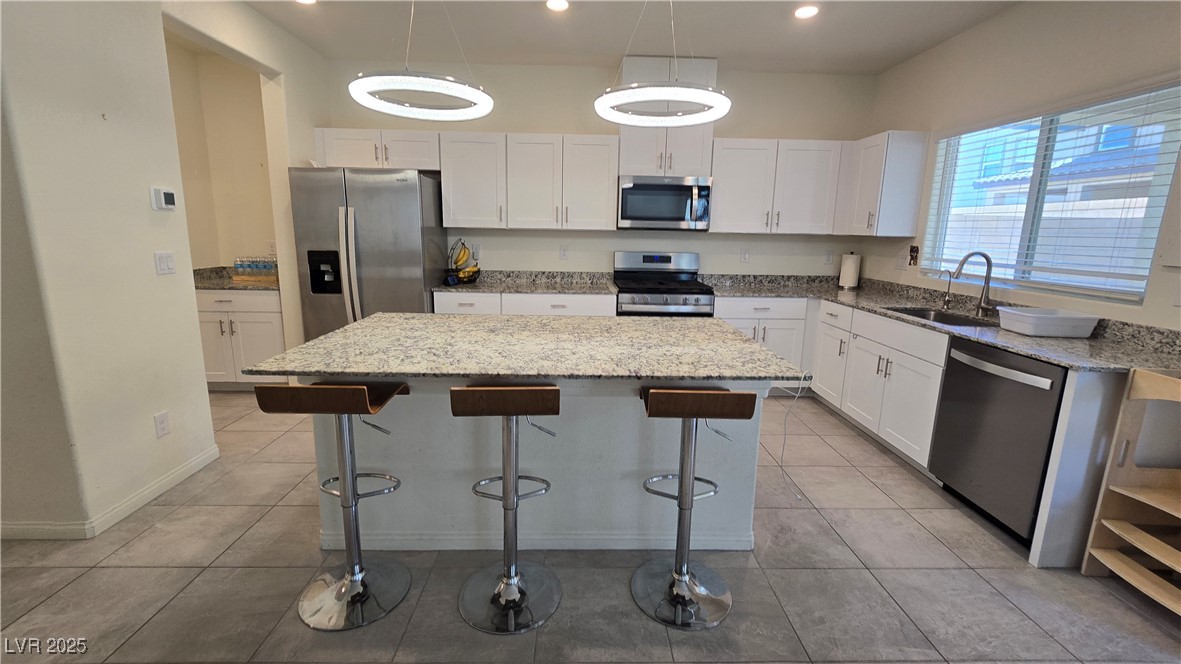10971 Meridian Fields Avenue Las Vegas, NV 89166 - Photo 25 of 66 Kitchen with appliances with stainless steel finishes, white cabinets, light stone counters, a kitchen island, and a breakfast bar area