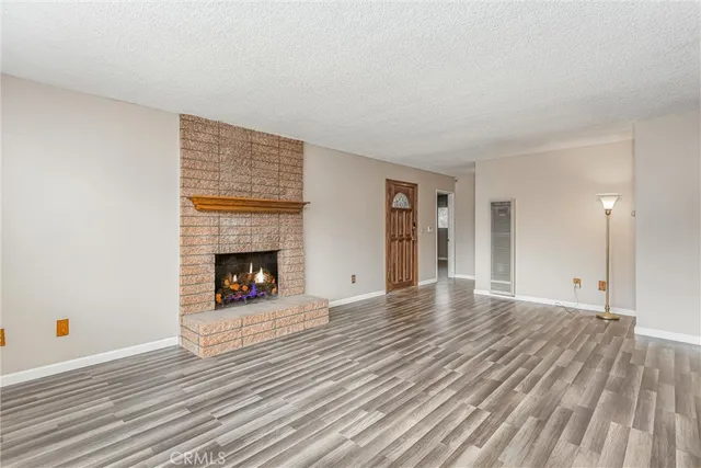 a view of an empty room with wooden floor fireplace and a window
