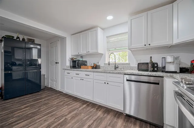 a kitchen with stainless steel appliances granite countertop a refrigerator a sink dishwasher and white cabinets with wooden floor