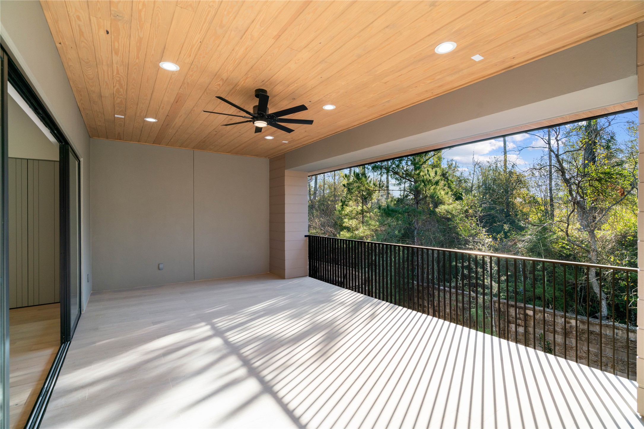 47 Pronghorn Place Spring, TX 77389 - Photo 35 of 44 This photo showcases a spacious covered patio with a wooden ceiling and ceiling fan, offering a serene view of lush greenery through a railing. Ideal for outdoor relaxation and gatherings.