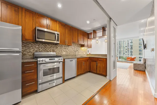 a kitchen with stainless steel appliances granite countertop a stove top oven a refrigerator a sink and dishwasher with wooden floor