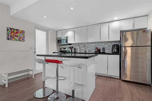 a kitchen with stainless steel appliances granite countertop a refrigerator a stove a sink and white cabinets with wooden floor