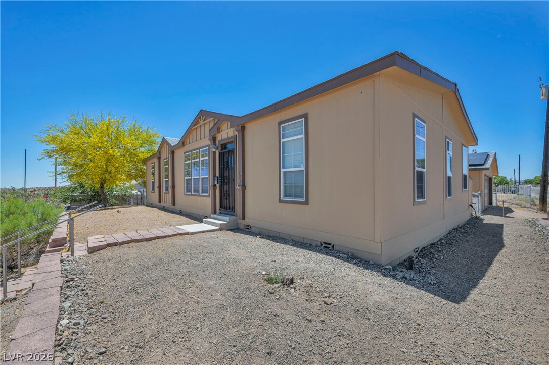 225 California Street Searchlight, NV 89046 - Photo 4 of 64 A modest desert home with a secure entryway and a vibrant yellow tree providing a splash of color against the arid landscape.