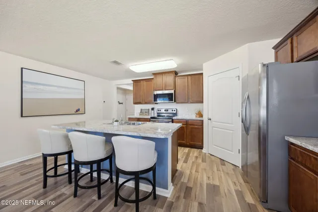 a kitchen with stainless steel appliances granite countertop a dining table chairs refrigerator and sink