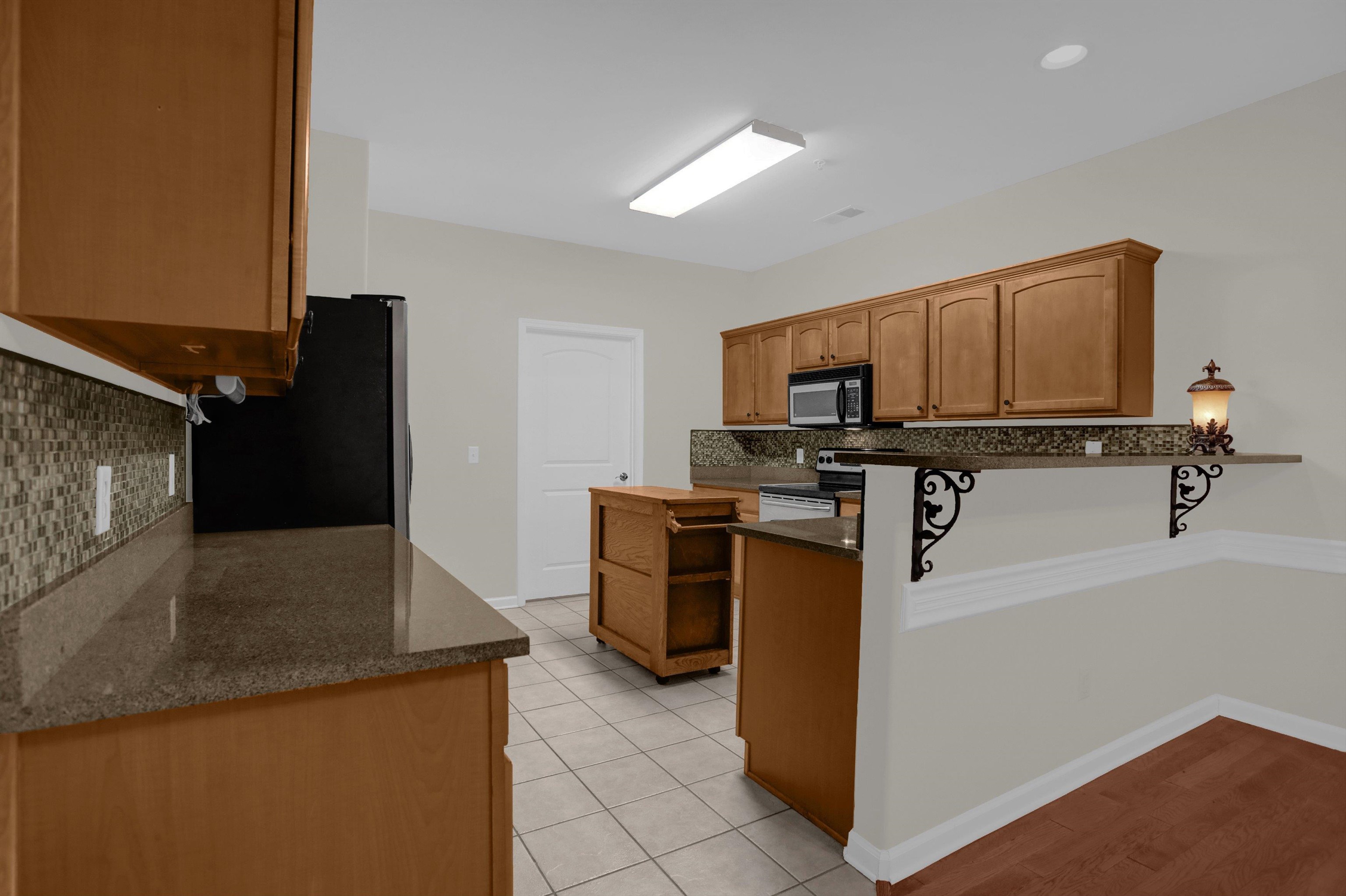34 Peyton Ridge Drive, Unit 21 Collierville, TN 38017 - Photo 18 of 37 Kitchen featuring wood-finish cabinetry, dark speckled countertops, and a mosaic tile backsplash