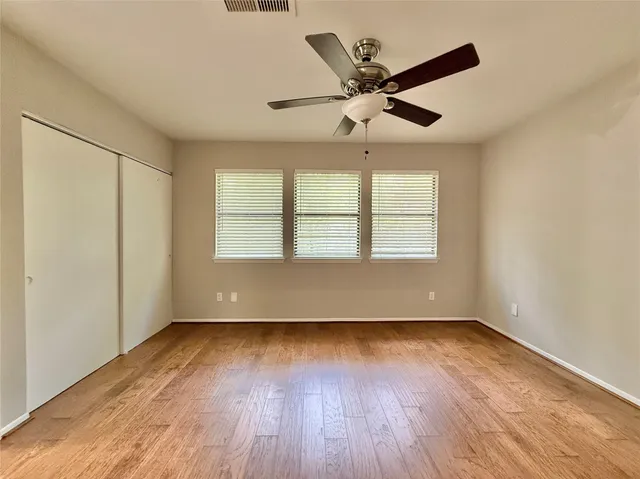 an empty room with wooden floor fan and windows