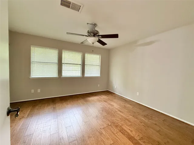 an empty room with wooden floor chandelier fan and windows