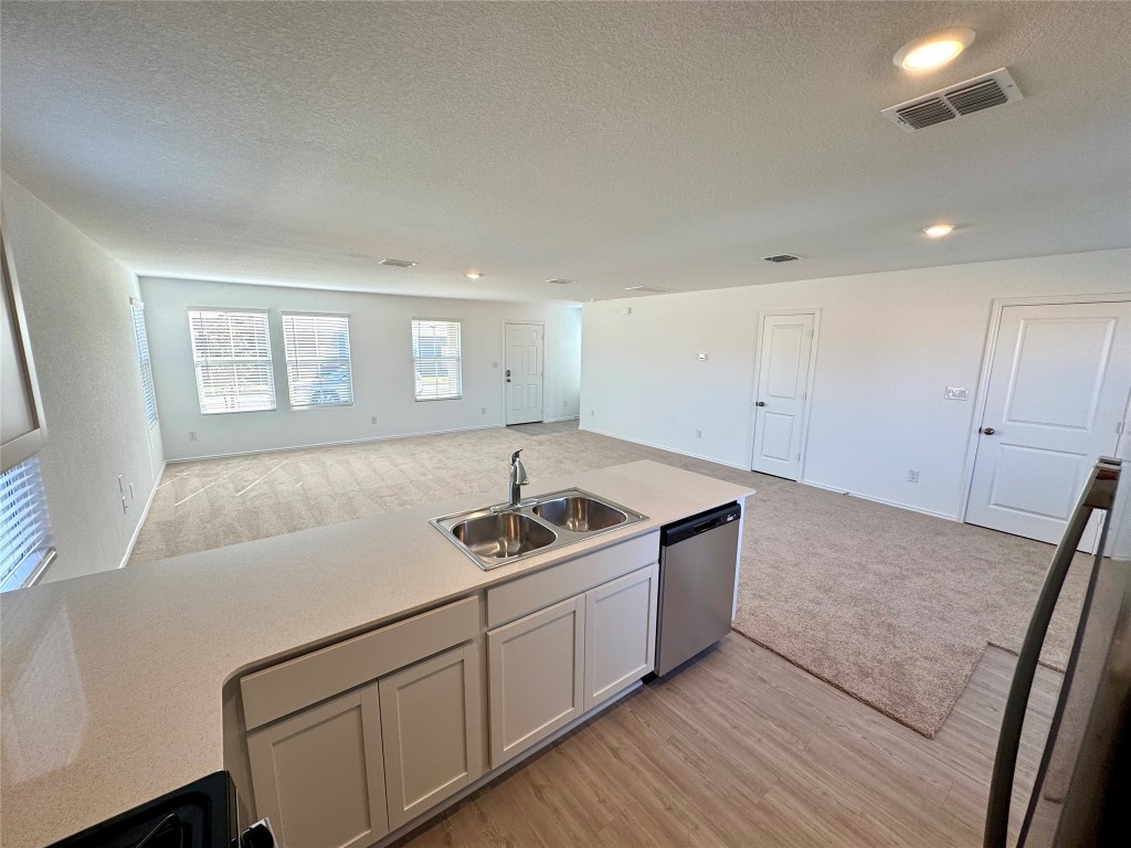 110 Haw Branch View Kyle, TX 78640 - Photo 15 of 15 Kitchen featuring open floor plan, light carpet, stainless steel dishwasher, white cabinetry, and a textured ceiling