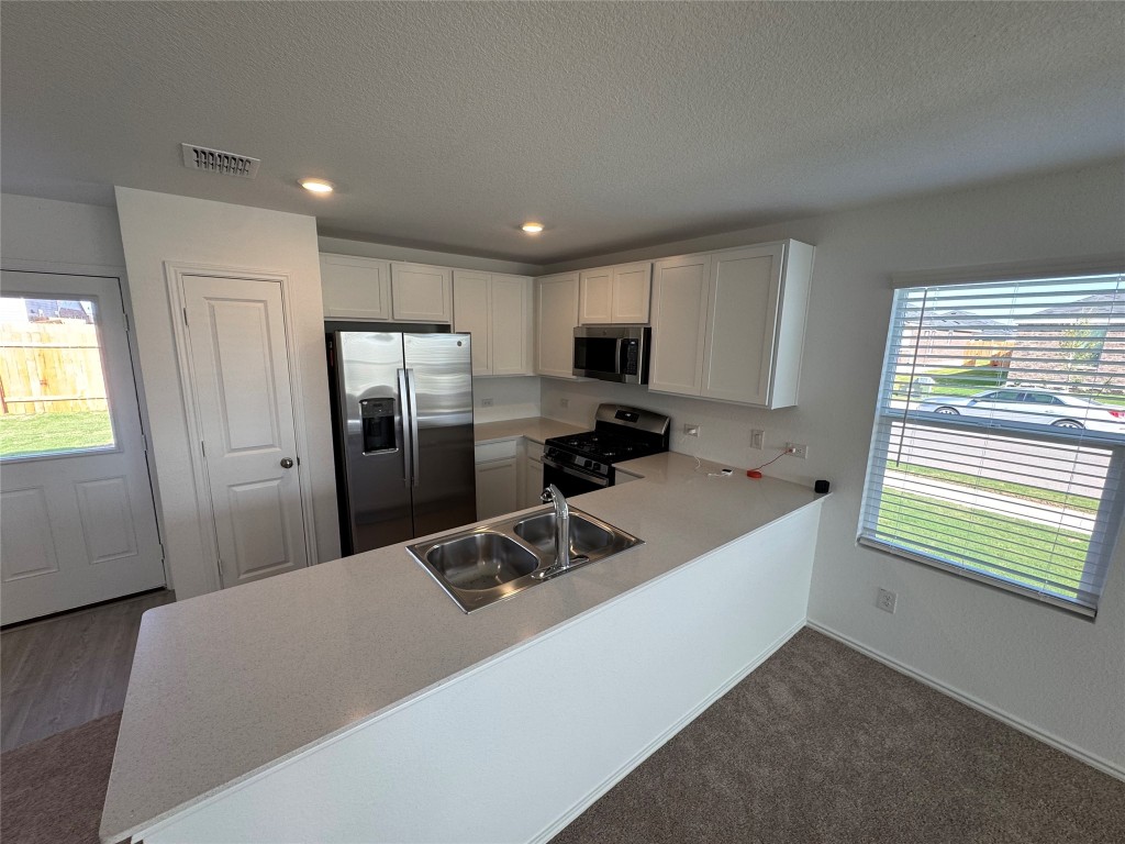 110 Haw Branch View Kyle, TX 78640 - Photo 6 of 15 Kitchen featuring plenty of natural light, light countertops, stainless steel appliances, white cabinets, and a textured ceiling