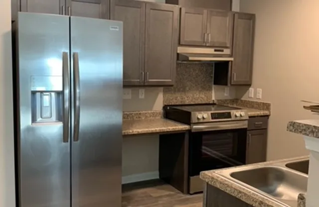 a kitchen with stainless steel appliances granite countertop a refrigerator a stove and a sink with wooden cabinet