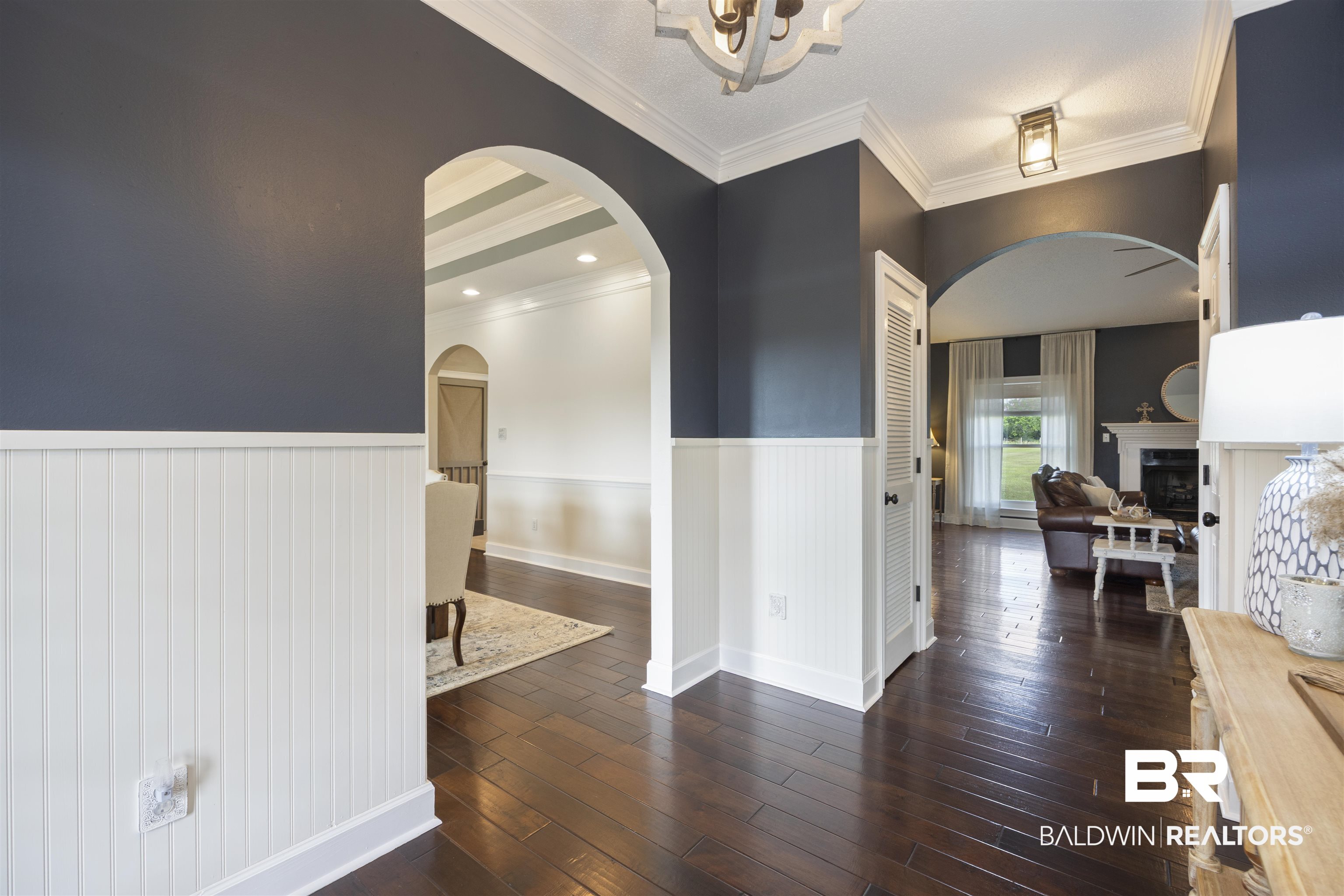 9855 Stucki Road Elberta, AL 36530 - Photo 10 of 54 Hallway with a wainscoted wall, dark wood-style floors, crown molding, arched walkways, and a chandelier