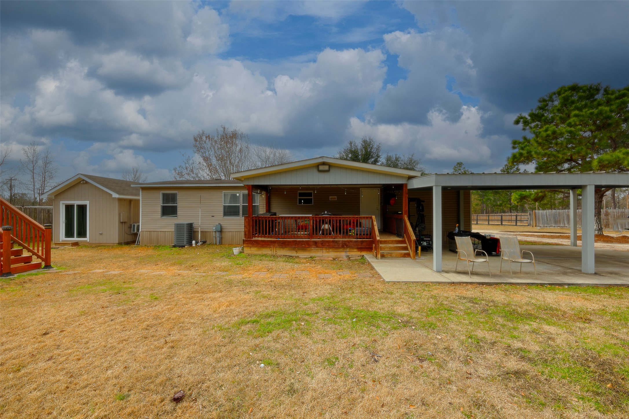 2373 Crockett Martin Road Conroe, TX 77306 - Photo 6 of 34 This photo shows a single-story home with a modest wooden porch and a covered carport. The yard is spacious and open, offering potential for landscaping. The sky is partly cloudy, adding a serene backdrop to the property.