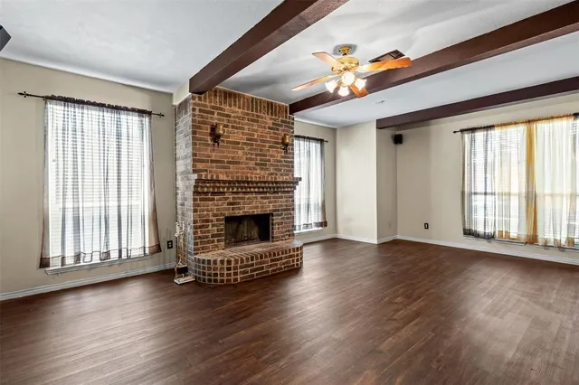 an empty room with wooden floor fireplace and windows