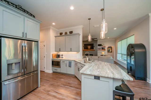 a kitchen with stainless steel appliances kitchen island granite countertop a refrigerator a sink dishwasher a stove and white cabinets with wooden floor