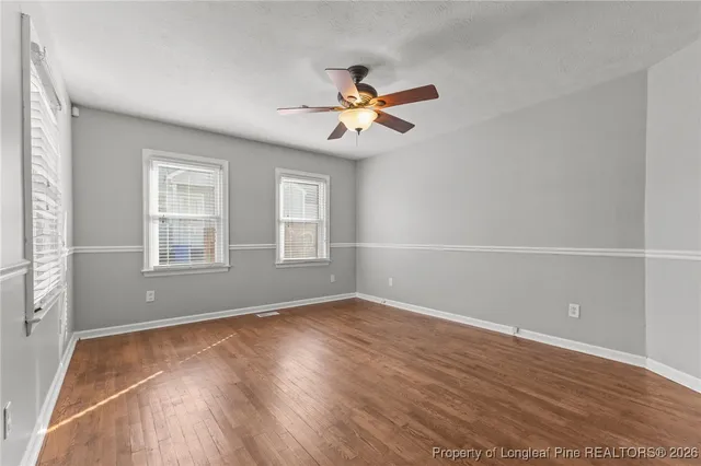 an empty room with wooden floor ceiling fan and windows