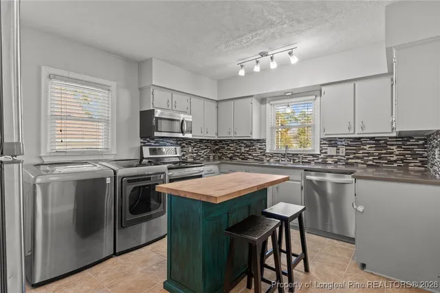 a kitchen with stainless steel appliances granite countertop a stove top oven a sink dishwasher a dining table and chairs with wooden floor