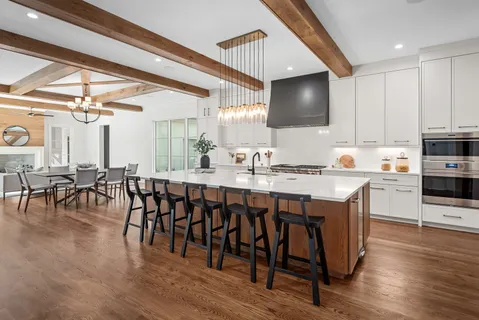 a open kitchen with stainless steel appliances granite countertop a stove top oven a refrigerator a dining table and chairs with wooden floor