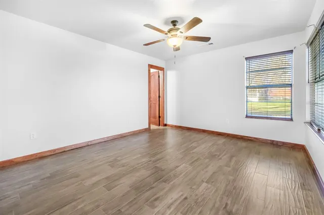 an empty room with wooden floor chandelier fan and windows
